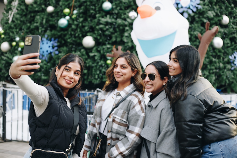 Four young women lean-in together to take selfie.