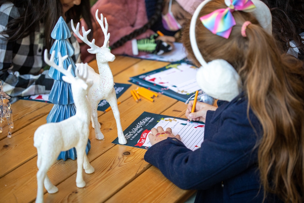 Young girl wearing big ear muffs is focused on writing her letter to Santa