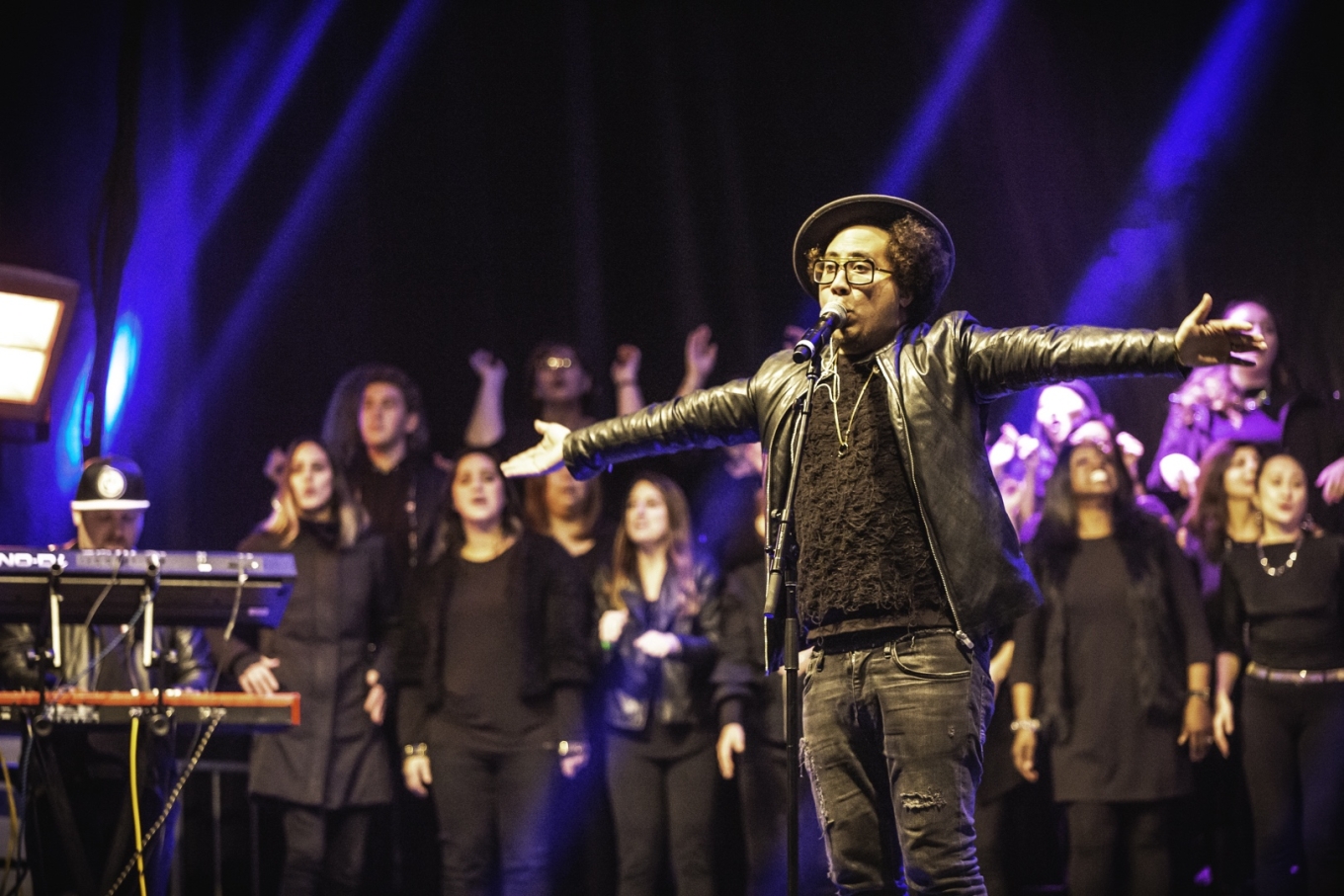 Choir on stage, with keyboardist, soloist stands at front with arms stretched wide